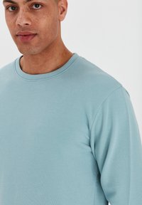 Lichtblauw sweatshirt met lange mouwen en een geribbelde ronde hals. De stof lijkt zacht met een gladde textuur en zonder zichtbare patronen.