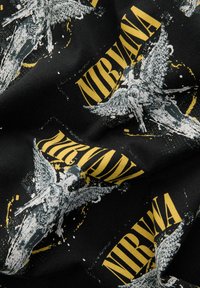 Fekete szövet, amelyen szárnyas alakok és a "NIRVANA" felirat sárgával látható grafikai minta található. A dizájn átfedéseket és texturált megjelenést tartalmaz.