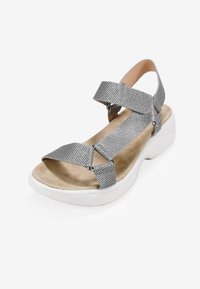 Sandalias de textil plateado con correas elásticas, plantilla acolchada beige y suela blanca gruesa. Cuenta con detalles metálicos en las correas.