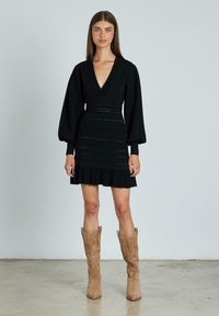 Mini abito nero con scollatura a V, lunghe maniche a sbuffo e orlo arricciato. Presenta dettagli texture lungo la vita e una silhouette aderente.