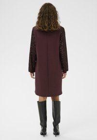 Abito bordeaux con maniche lunghe coperte di paillettes, tessuto liscio, lunghezza fino al ginocchio, abbinato a stivali in pelle nera al ginocchio.