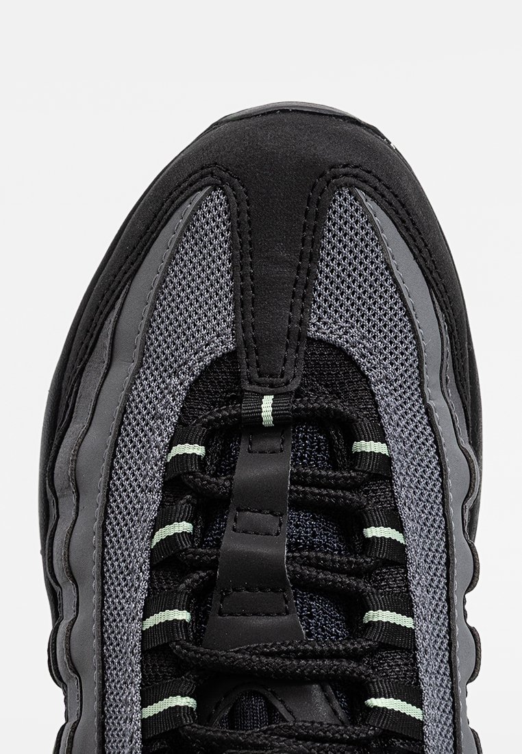 Chaussure de sport noire et grise en matériaux synthétiques et en mesh, avec un dessus texturé, un bout rond et des lacets contrastés avec des accents verts.