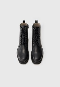Botas de cuero negro hasta el tobillo con cordones y cremallera lateral, con una textura suave y diseño de punta redonda. Incluye una lengüeta en la parte trasera.