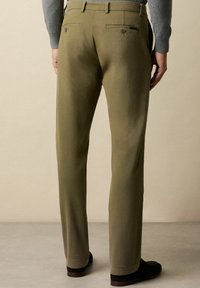 Oliwkowe spodnie z bawełnianej mieszanki o prostym kroju, z dwiema tylnymi kieszeniami i bezszwowym pasem; zestawione z ciemnymi butami.