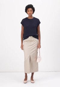 Marineblaues, gestricktes Shirt mit kurzen Ärmeln, beiger Cargo-Rock mit Schlitz vorne, hellrosa Handtasche und passenden Ballerinas. Sauberes Design und neutrale Farben.