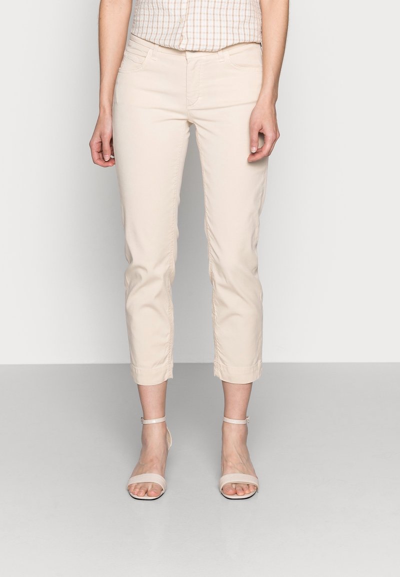 Pantalones cortos beige con textura suave, corte ajustado y puños remangados. Combinados con sandalias de tiras de color claro.