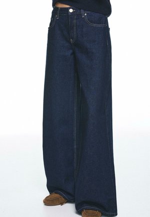 Dunkelblaue Jeans mit weitem Bein aus Denim, ausgestattet mit Fronttaschen, einem Knopfleistenverschluss und kontrastierender Naht für zusätzliche Details.