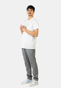 White cotton t-shirt with a small logo, gray textured trousers, and white sneakers with light blue accents. Individual stands upright.