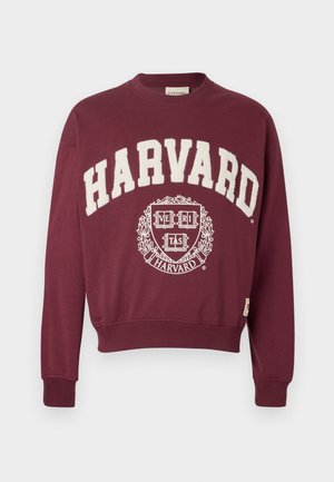 Maroon sweatshirt with "HARVARD" printed in white, featuring a circular emblem with "VERITAS" and decorative accents at the center.