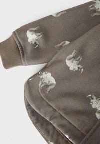 Tessuto di felpa marrone con un motivo ripetuto di rinoceronti. Polsini e orlo a coste con una texture liscia e dettagli di cucitura sottili.