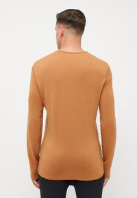 Chemise à manches longues de couleur marron chaud, fabriquée en tissu doux avec un col rond et une coupe ajustée. Coutures minimales et texture lisse.