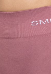 Mauve leggings met een gewatteerde tailleband met het witte "SM" logo. De stof is glad en elastisch, met een getailleerde pasvorm.