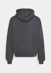 Sudadera gris oscuro con capucha ajustable, puños y dobladillo acanalados. Presenta un logo en la parte posterior cerca del cuello. Tela suave y texturizada.
