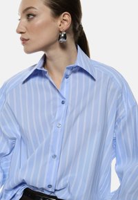 Camicia a righe blu con vestibilità rilassata, design a bottoni e colletto classico. Presenta righe azzurre e bianche, bottoni a contrasto.