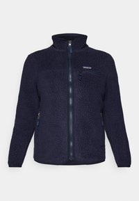 Giacca in pile blu scuro con colletto alto, chiusura con zip, tasche laterali e tasca sul petto. Presenta un tessuto testurizzato e il logo del marchio.