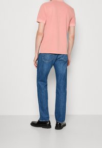 T-shirt rose pâle à manches courtes associé à un jean en denim bleu et des chaussures noires. Le tissu semble lisse et la coupe est décontractée.