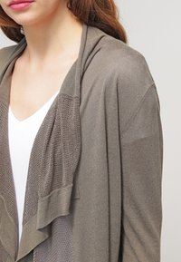 Lätt, gråbrun cardigan med öppen front, texturerad stickning och långa, flödande ärmar. Material av bomullsblandning.