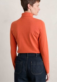 Maglione a maniche lunghe con collo alto di un vivace arancione, realizzato in un tessuto morbido e elastico. Abbina a un paio di jeans in denim scuro con tasche posteriori.