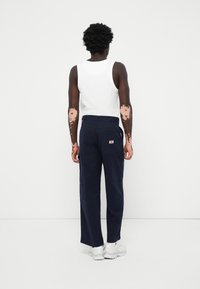 Calças de carga navy com vários bolsos, um ajuste ligeiramente solto e um logo tecido, combinadas com uma t-shirt branca sem mangas e ténis brancos.