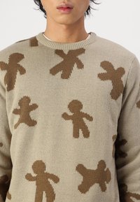 Beige knitted sweater featuring brown gingerbread man patterns, with a round neckline and a soft texture.