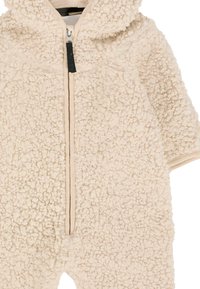 Tutina in pile di colore crema con superficie testurizzata. Presenta una zip frontale e un cappuccio, con maniche corte e polsini elastici.