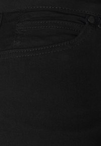 Tecido de denim preto em close-up, apresentando costuras visíveis, detalhes dos bolsos e uma textura suave. Design minimalista sem padrões notáveis.