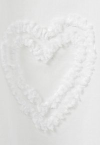 Weißer Stoff mit einem strukturierten Herzdesign aus flauschigem Material, umrandet von einem Rüschensaum, vor einem glatten weißen Hintergrund.