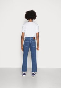 Blauwe jeans met hoge taille en een rechte pijp, voorzien van twee achterzakken, gecombineerd met een effen wit t-shirt. Het materiaal lijkt denim te zijn.
