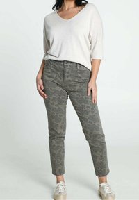 Haut beige clair à manches courtes avec décolleté en V, associé à un jean vert olive à motifs. Motif cachemire texturé, coupe slim, chevilles retroussées.