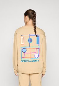 Beige oversized sweatshirt featuring a colorful geometric design on the back, with accents of blue, purple, and text reading "SPORTIVAMENTE."