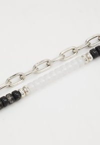 Bracelet en chaîne argentée avec des perles cylindriques noires et blanches alternées, agrémenté d'accents réfléchissants entre les perles.