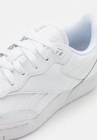 Fehér bőr sportcipő textúrált felülettel, fűzőkkel, párnázott bokarésszel, Reebok logóval és világoskék kontrasztos talpbetéttel.