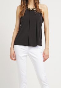 Top nero senza maniche con un design frontale plissè, accentuato da una collana d'oro circolare. Abbinato a pantaloni bianchi, dalla texture liscia.