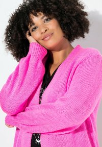 Cardigan aperto lavorato a maglia di un vivace colore rosa, con maniche lunghe e una vestibilità ampia. Tessuto strutturato con polsini a coste.
