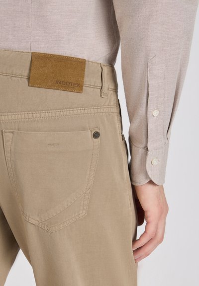 Pantalones caqui de corte recto, fabricados en tejido de algodón. Presentan un parche de cuero marrón con la etiqueta "INCOTEX" y detalles sutiles en los bolsillos traseros.