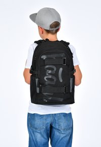 Černý batoh s šedými akcenty a velkým grafickým textem. Obsahuje několik přihrádek, nastavitelné popruhy a robustní design.