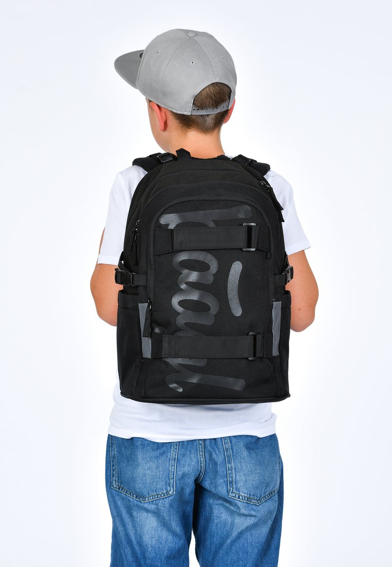 Černý batoh s šedými akcenty a velkým grafickým textem. Obsahuje několik přihrádek, nastavitelné popruhy a robustní design.