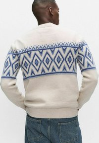 Vaaleankermanvärinen neulepaita, jossa on geometrinen sininen timanttikuosi. Varustettu resoroiduilla kalvosimilla ja helmalla, pehmeästä materiaalista neulottu. Yksinkertainen pyöreä kaulus.