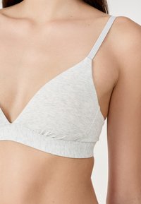 Light gray cotton triangle bralette with thin white straps, gathered at the band for fit, featuring a smooth texture and a minimalist design.