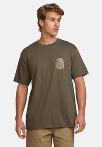 Olive green short-sleeve t-shirt made of cotton, featuring a cream graphic design on the left chest. Relaxed fit with a crew neckline.