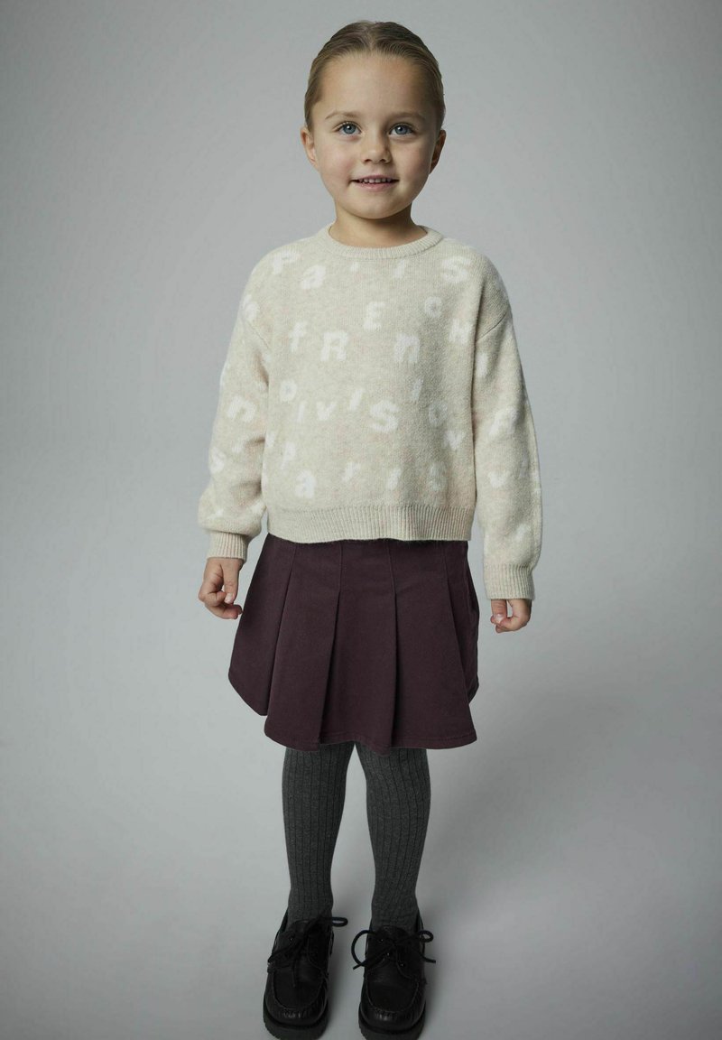 Maglione azzurro beige lavorato a maglia con lettere bianche; gonna plissettata di prugna scura; collant grigi a costine; scarpe nere con lacci. Outfit semplice e casual.