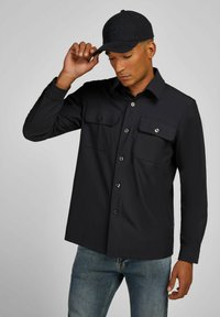 Zwarte button-up shirt met twee borstzakken, lange mouwen en een rechte zoom. Gekocht met een blauwe jeans en een zwarte pet.