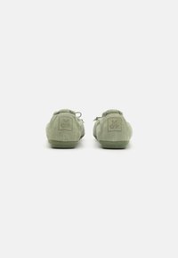 Chaussures en daim vert avec une forme arrondie, présentant un laçage, un col rembourré et un logo en relief sur le talon.