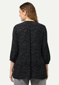 Blusa nera a fantasia con maniche a tre quarti, orlo arrotondato e tessuto strutturato. Design floreale morbido in tonalità più chiare che aumenta l'interesse visivo.