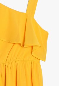 Żółta bezrękawnikowa sukienka z falbaną na dekolcie i elastycznym, marszczonym pasem.