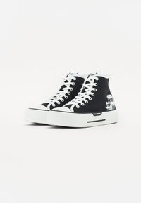 Høye sneakers laget av svart lerret med hvite gummisåler og snørebånd, med grafisk aksent på den ene siden og logo på tungen.