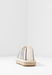 Espadril med en krämfärgad textilöverdel med marinblå ränder, jute rep-sula och kontrasterande bakflik för enkel påtagning. Mjuk, texturerad finish.
