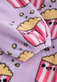 Fialová fleecová tkanina s potlačou popcornu, na ktorej sú zobrazené karikatúry popcornových krabičiek, žlté zrná a mäkká štruktúra. Viditeľný detail na elastických manžetách.