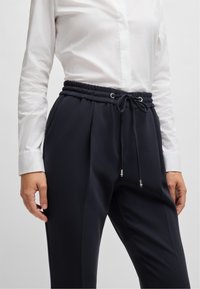 Marinebroeken met een elastische tailleband, verstelbaar trekkoord en zijzakken. De stof is glad en heeft een getailleerd ontwerp.