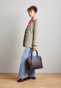Sort læderhåndtaske med rundede håndtag, lynlåslukning og subtile hardwaredetaljer, parret med en ternet blazer og brede denimjeans.